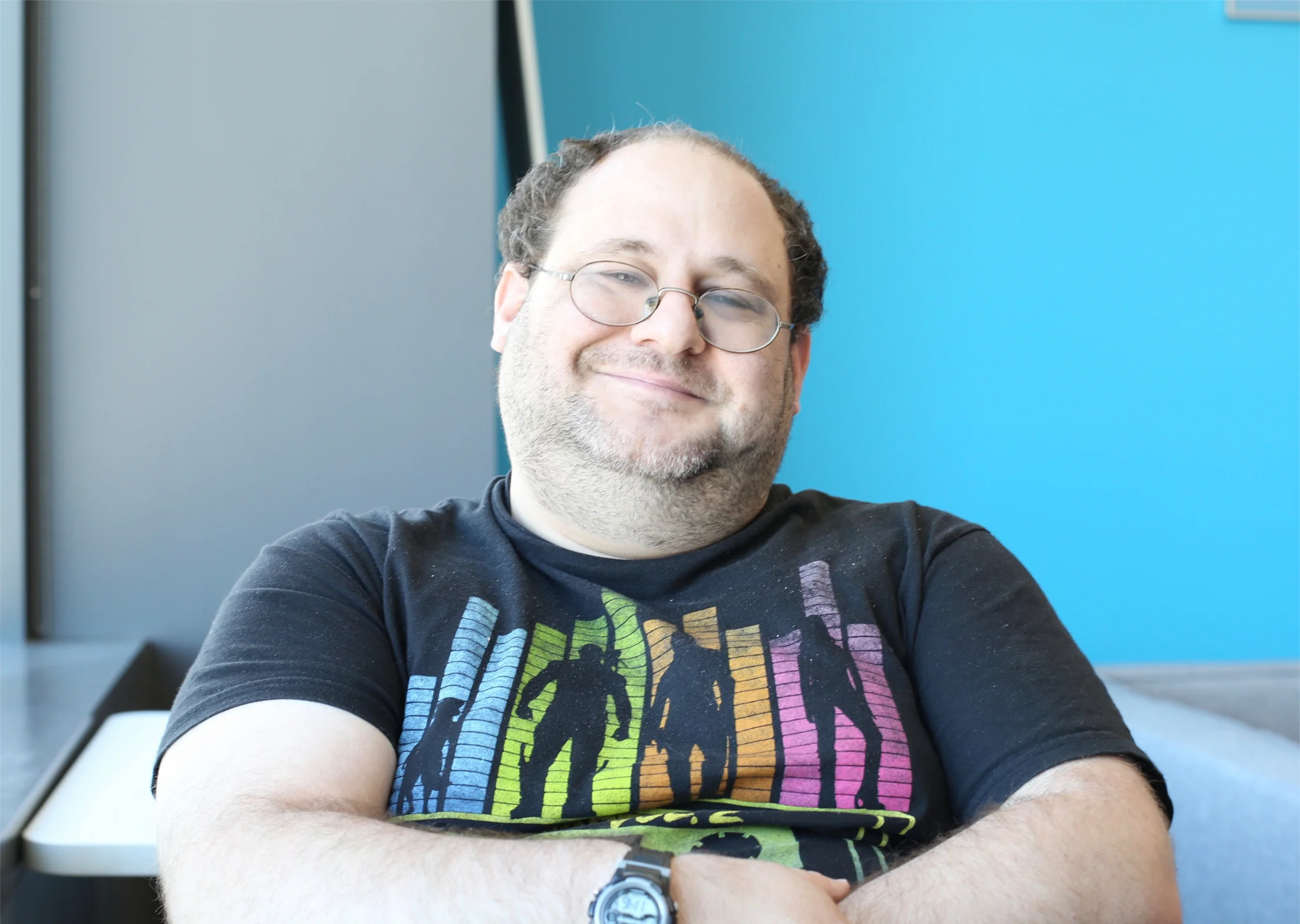 Moshe sitting down, head slightly to the side. His t-shirt has Guardians of the Galaxy silhoutes against a background of sound visualization bars.